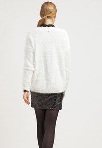 Vit luddig tröja med avslappnad passform, med långa ärmar och rund halsringning. Kombinerad med en svart paljettminikjol.
