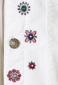 Tejido blanco con un botón decorativo dorado y patrones florales multicolores bordados con pequeños lentejuelas reflectantes.