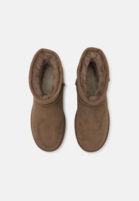 Bottes chelsea en suede marron avec une douce doublure en fourrure, dotées d'un bout rond et d'une fermeture éclair sur le côté pour un enfilage facile. Texture lisse sur le dessus.