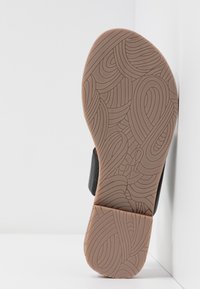 Semelle d’une chaussure noire avec une semelle extérieure épaisse en caoutchouc marron présentant des motifs complexes de rainures en tourbillon pour l’adhérence.