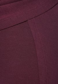Close-up of folded dark purple fabric showing fine knit texture and visible stitching along the seam.