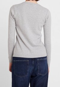 Harmaa, pitkähihainen neule pyöreällä kaula-aukolla. Pehmeä rakenne, istuva malli, yhdistetty tummansinisiin farkkuihin, joissa on taskuyksityiskohtia.