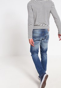 Camisa de manga larga a rayas con vaqueros azules, con un acabado desgastado, diseño de cinco bolsillos y zapatillas de suela de goma.