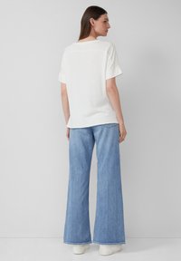 Witte katoenen t-shirt met opgerolde mouwen, gecombineerd met lichtblauwe brede denim jeans en witte platform sneakers, gezien vanuit de achterkant.