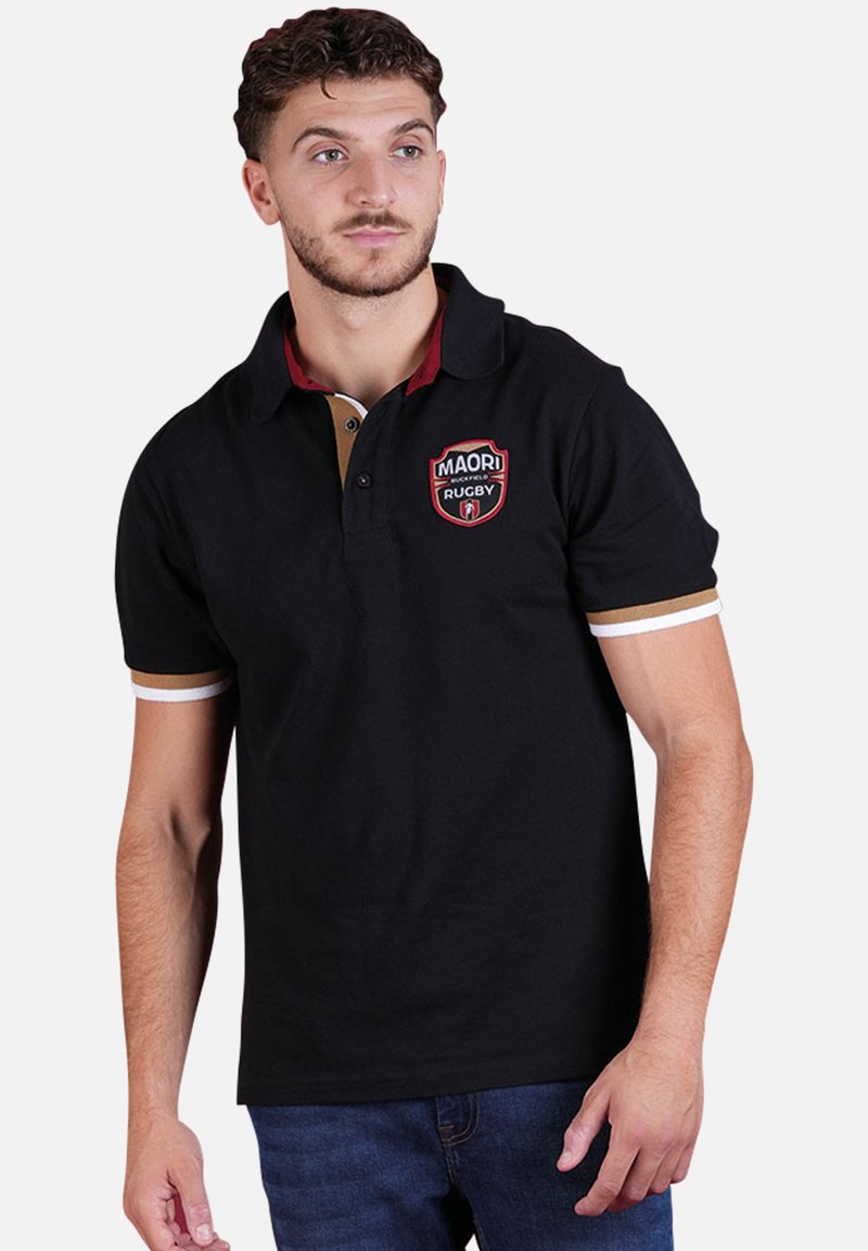 Polo noir avec des accents rouges et dorés, manches courtes, col, et un patch logo de rugby sur la poitrine. Matériau en coton, texture lisse.