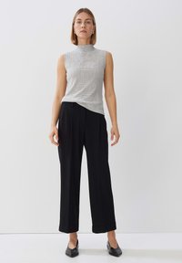 Grijze mouwloze top met een hoge halslijn en een subtiel patroon, gecombineerd met hoge taille zwarte broek en puntige zwarte schoenen.