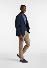 Marinblå blazer över en blå t-shirt, kombinerad med ljusbruna byxor och marinblå sneakers med bruna sulor. Blazern har två framfickor.