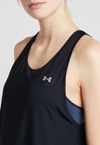 Czarna sportowa koszulka na ramiączkach z okrągłym dekoltem, z odblaskowym logo. Pod spodem widać niebieski, teksturowany stanik sportowy.