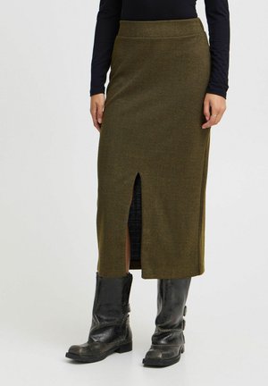 Olijfgroen herringbone gebreide midi-rok met een split aan de voorkant, gecombineerd met hoge zwarte gebreide laarzen. Soepel tailleband, zonder zichtbare sluitingen.