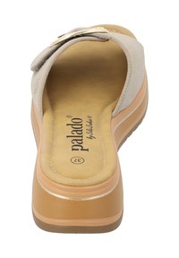 Sandalia slip-on beige con parte superior de ante suave, plantilla acolchada y un ligero tacón. Presenta un acento de hebilla en tono dorado.