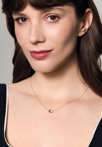 Srebrny naszyjnik z okrągłym wisiorkiem ozdobionym małym kamieniem akcentującym, prezentowany na skórze z ciemnym topem. Prosty i elegancki design.