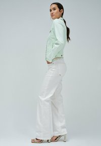 Chaqueta de denim verde menta con un diseño ajustado, pantalones blancos de cintura alta y tacones beige con tiras. Tela suave con un hardware mínimo.
