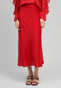 Jupe midi rouge en tissu léger, avec une texture douce et une silhouette en A, associée à des sandales à lanières marron.