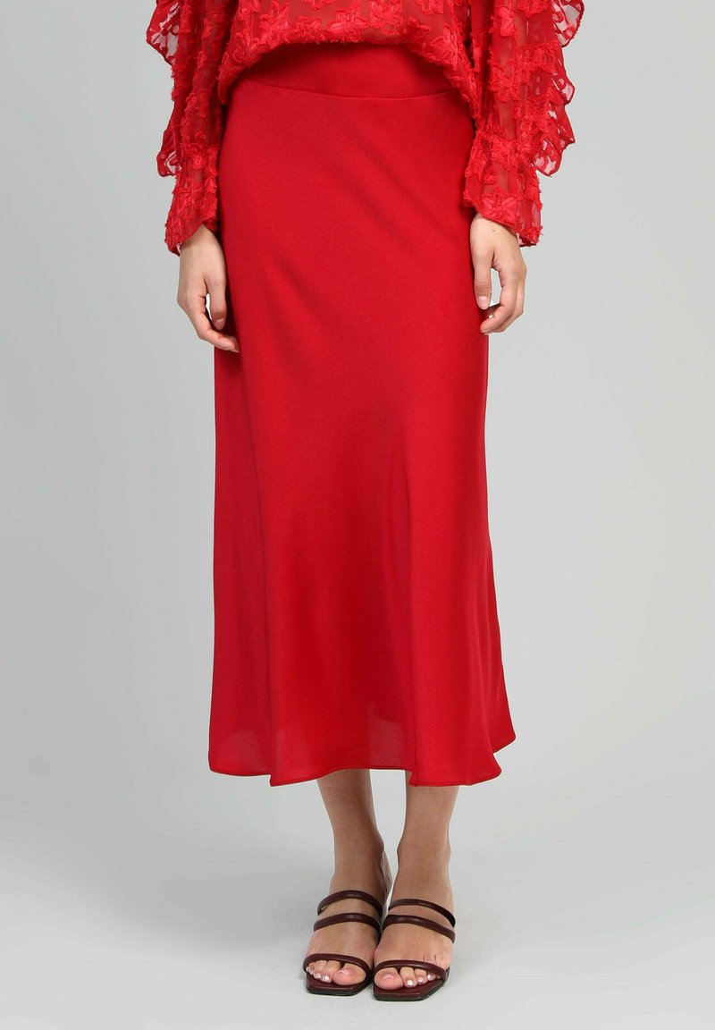 Jupe midi rouge en tissu léger, avec une texture douce et une silhouette en A, associée à des sandales à lanières marron.