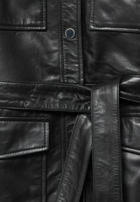 Veste en cuir noire avec boutons-pression à l'avant, taille ceinturée et poches rectangulaires cousues.