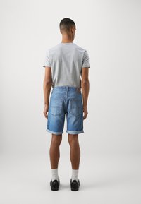 Grå kortermet t-skjorte kombinert med denimshorts med rullet kant. Shortsen er lyseblå med to baklommer og en lærlapp.