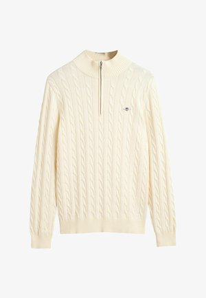 Pull en tricot torsadé de couleur crème avec un col montant et une fermeture à demi-zip ; il présente des poignets et un ourlet côtelés, une texture douce et un accent logo.