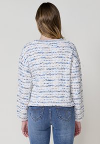 Pull en mélange de coton avec une base texturée blanche ornée de rayures bleues et beiges, col rond et coupe ample. Associé à un jean bleu classique.