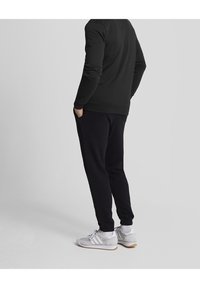 Sort sweatshirt med lange ærmer og ribbede manchetter, parret med mørke joggers og hvide sportssko. Enkel, afslappet design.