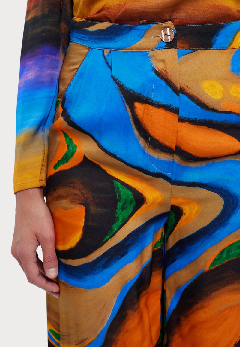 Wielokolorowa tkanina z wyrazistymi abstrakcyjnymi wzorami w niebieskim, pomarańczowym, zielonym i brązowym kolorze. Posiada zapięcie na guziki i plisowanie w talii.