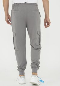 Grå cargobyxor i mjukt material, med elastisk midja, sidofickor och avsmalnande muddar, bärs med vita sneakers.