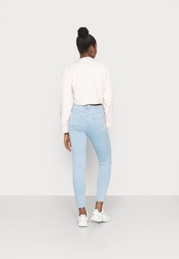 Jeans skinning azul claro com cintura alta, combinados com um sweatshirt cropped rosa e tênis brancos, vistos de costas.