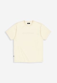 Crème-kleurig T-shirt met korte mouwen en ronde hals, met subtiele tekst "Butcher of Blue" gedrukt op de borst, plat gelegd op een witte achtergrond.