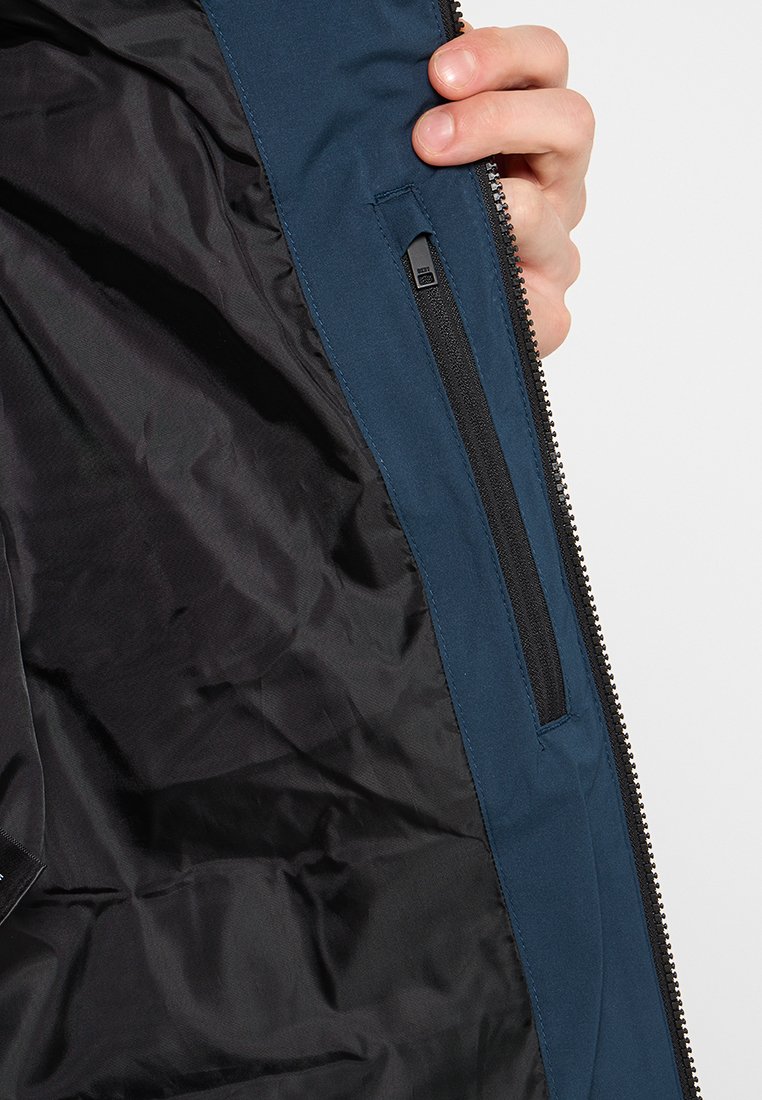 Marineblauw jasje met zwart binnenwerk, voorzien van een ritszak en een soepele textuur. De blootgestelde rits langs de rand voegt contrast toe.
