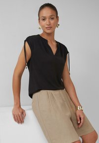 Schwarzes Kurzarmoberteil mit V-Ausschnitt und Kordelzugakzenten an den Schultern, kombiniert mit beigen High-Waist-Shorts.