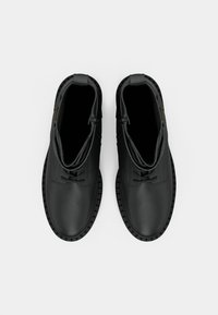 Bottines noires à lacets avec un dessus en cuir lisse, bout rond et semelle en caoutchouc texturée. Dotées de coutures discrètes et d'un accent doré.