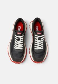 Sneaker in pelle nera con lacci bianchi, dettagli rossi e una suola in gomma robusta. Presenta un design con superficie liscia e testurizzata.