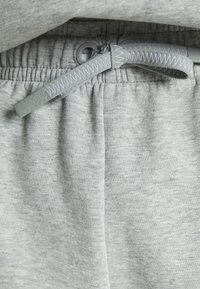 Gros plan de la taille d’un pantalon de survêtement gris avec un cordon gris noué présentant une couture en zigzag blanche.