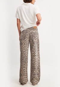 Beige en bruine wijde broek met luipaardprint en een gladde textuur, met een merklabel op de tailleband en achterzakken.