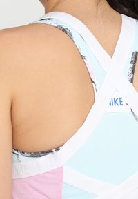 Jasnoniebieska sportowa koszulka bez rękawów z różowymi akcentami, z wycięciem na plecach oraz białymi elastycznymi ramiączkami z logo, ozdobionymi wzorem kwiatowym.