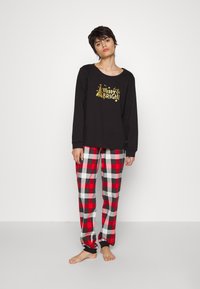 Sweatshirt noir à manches longues avec un graphisme "Merry & Bright" et des accents dorés, associé à un pantalon de pyjama à carreaux rouge, blanc et noir.