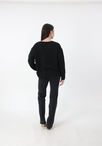 Zwarte gebreide trui met een losse pasvorm en ribgebreide zoom, gecombineerd met zwarte rechte broek en beige hoge hakken.