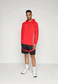 Rød Nike hettegenser med logo på brystet, svarte shorts med røde detaljer, hvite sneakers og hvite sokker. Glatt tekstur, sporty design.