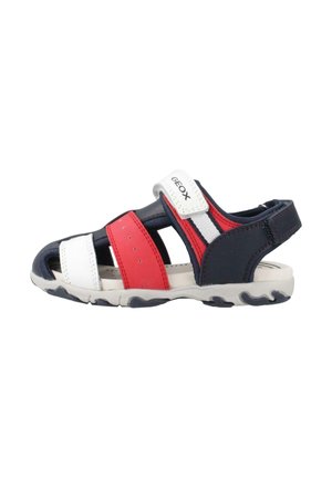 Sandalo sportivo per bambini con cinturini rossi, bianchi e blu navy, chiusura a strappo e suola in gomma per uso esterno.