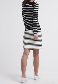 Schwarz-weiß gestreiftes Langarmoberteil kombiniert mit einem weißen Rock mit horizontalen Streifen, getragen mit weißen Turnschuhen.