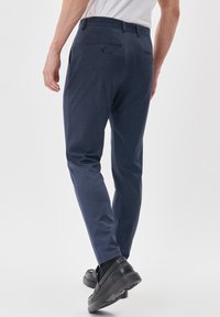 Laivastonsininen muotikkaat housut, joissa on sileä pinta, kapea istuvuus ja takataskut. Yhdistetty mustiin kenkiin, jotka korostavat minimalistista muotoilua.