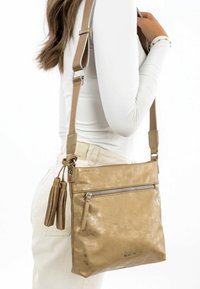 Metallic gold crossbody bag made of faux leather, featuring a zippered pocket, tassel accents, and adjustable straps. Smooth texture.