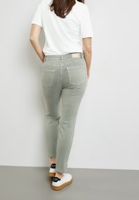 Světlé zelené džíny s přiléhavým střihem, pěti kapsami a jednoduchým designem. Doplněné bílými teniskami s černými akcenty.