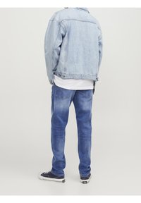 Chaqueta de mezclilla azul clara combinada con jeans azul medio. El conjunto incluye una camisa blanca debajo y zapatillas negras.