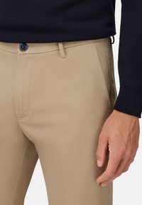 Beige dress pants with a smooth texture, featuring a tailored fit, front pockets, and a dark button at the waist.
