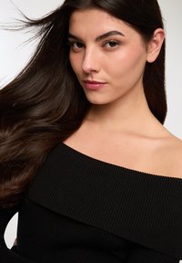Top nero a costine senza spalle con ampia scollatura, texture liscia e design aderente. I capelli cadono dolcemente sulla spalla.