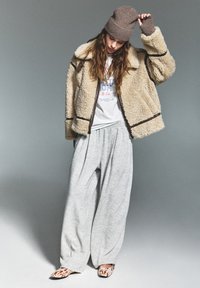 Fluffy crèmekleurige jasje met bruine accenten, grijze oversized sweatpants en dierenprint instappers. Bruine gebreide beanie en casual graphic t-shirt.