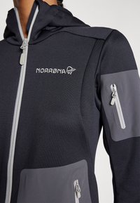 Ciemnoszara długosleeve'owa kurtka z kapturem z jasnoszarymi akcentami, zapinanymi na zamek kieszeniami i haftowanym logo na klatce piersiowej. Teksturowana tkanina.