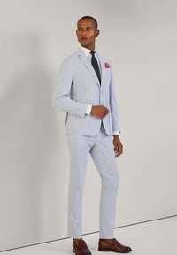 Completo a righe blu chiaro con blazer aderente e pantaloni. Camicia bianca, cravatta blu navy con pois e fazzoletto rosa. Scarpe marroni.