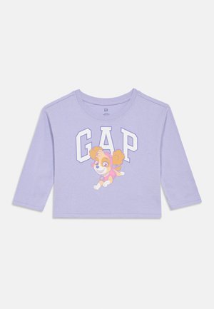 Lila, hosszú ujjú, cropped póló, rajta egy rajzfilm kutyával és nagy betűkkel a "GAP" felirattal. Puha, pamut anyag, lekerekített nyakkal.