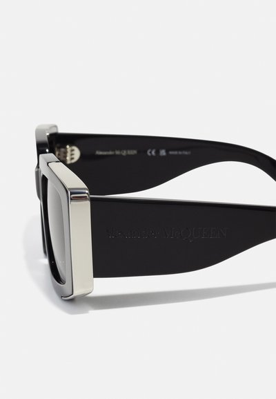 Ochelari de soare negri cu o ramă pătrată, accente metalice pe margini și branding gravat pe braț. Finisaj din plastic neted.